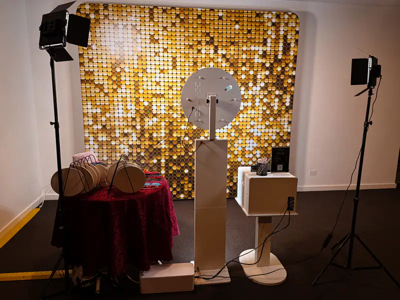 The white booth set up in front of a gold sequin backdrop with studio lights