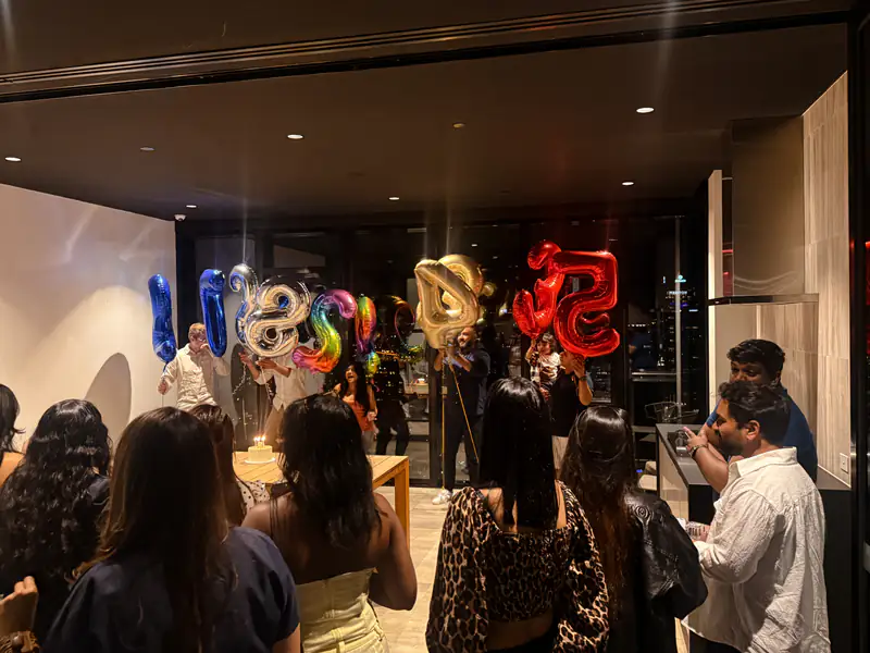 Guests crowding around at a birthday party with number balloons